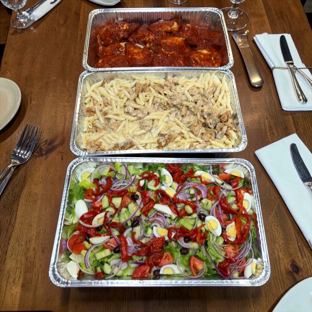 Full catering spread with chicken parm, pasta, and salad